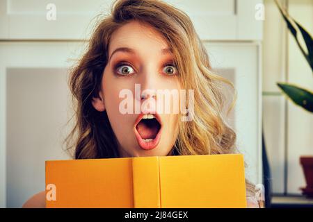 young shocked college woman with book in hands looking at camera library book store Stock Photo