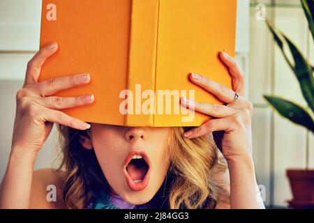 young shocked college woman with book in hands covering face library book store Stock Photo