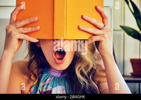 young shocked college woman with book in hands covering face library book store Stock Photo