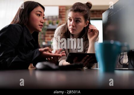 Blockchain developing engineer using high technology software to defend database system. Unsure asian programming expert asking colleague about generated bug report file. Stock Photo