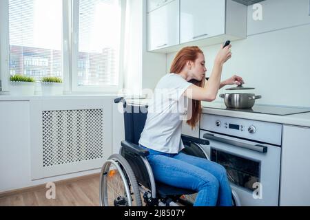 disabled redhaired ginger woman in wheelchair preparing meal in kitchen Stock Photo