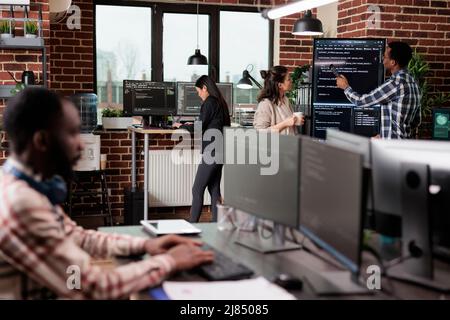 Tech engineers team leader pointing out mistake in application source code. Software developers standing near vertical screen talking about interface bug and slow rate of processing data. Stock Photo