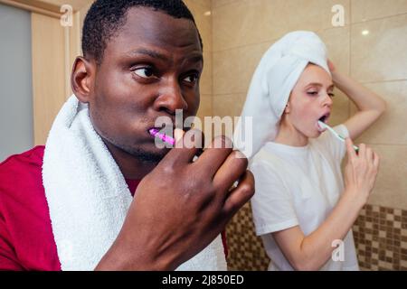 african american man and woman with wet hair wrapped on towel after shower whitening teeth before going to work Stock Photo