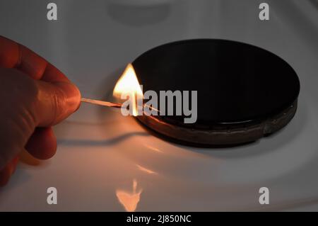 No gas of the home kitchen stove due to the crisis and natural gas import shutdown. A hand sets fire to gas stove that has no gas with a match. Stock Photo