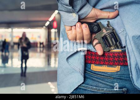 A man robs women. Armed robbery on the street. The concept of street crime. A man's hand pulls a loaded revolver out of his jeans. Stock Photo