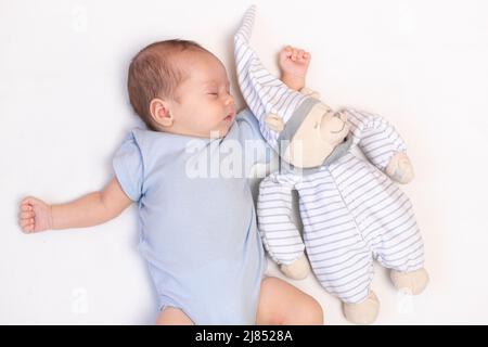 The baby is lying in a crib with a teddy bear . The baby is 0-3 months old. A calm sleeping baby. Healthy baby sleep. An article about toys for kids. A soft toy. Copy Space Stock Photo