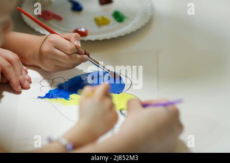 Bucharest, Romania - May 9, 2022: Shallow depth of field (selective focus) details with Ukrainian refugee children drawing Ukrainian heart shaped flag Stock Photo