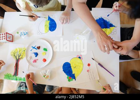 Bucharest, Romania - May 9, 2022: Shallow depth of field (selective focus) details with Ukrainian refugee children drawing Ukrainian heart shaped flag Stock Photo