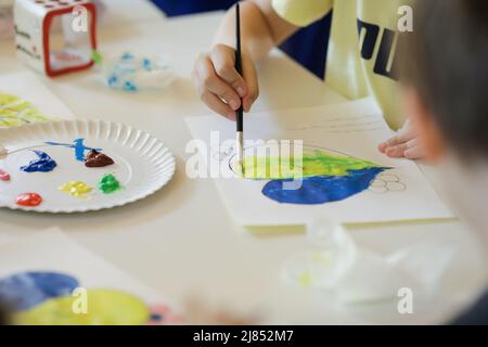 Bucharest, Romania - May 9, 2022: Shallow depth of field (selective focus) details with Ukrainian refugee children drawing Ukrainian heart shaped flag Stock Photo