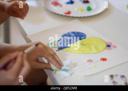 Bucharest, Romania - May 9, 2022: Shallow depth of field (selective focus) details with Ukrainian refugee children drawing Ukrainian heart shaped flag Stock Photo