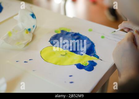 Bucharest, Romania - May 9, 2022: Shallow depth of field (selective focus) details with Ukrainian refugee children drawing Ukrainian heart shaped flag Stock Photo