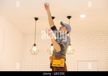 Young electrician installing smoke detector on ceiling Stock Photo