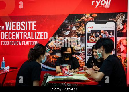 People work on promotional materials at a booth promoting a decentralized food review platform at Thailand Crypto Expo 2022. People attend Thailand Crypto Expo 2022 at Bangkok International Trade & Exhibition Centre (BITEC) in Bangkok. The convention, calling itself the "The largest Crypto Expo in South East Asia," happens during a moment of panic for investors worldwide due to a cryptocurrency market crash, with popular Terra Luna (LUNA) losing 99% of its value overnight and Bitcoin (BTC) losing 2%, taking it to $28,379.26, a 16-month low. Stock Photo