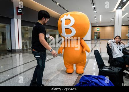 A worker helps to put the headpiece on top of a performer in a Bitcoin (BTC) costume at Thailand Crypto Expo 2022. People attend Thailand Crypto Expo 2022 at Bangkok International Trade & Exhibition Centre (BITEC) in Bangkok. The convention, calling itself the "The largest Crypto Expo in South East Asia," happens during a moment of panic for investors worldwide due to a cryptocurrency market crash, with popular Terra Luna (LUNA) losing 99% of its value overnight and Bitcoin (BTC) losing 2%, taking it to $28,379.26, a 16-month low. (Photo by Matt Hunt/SOPA Images/Sipa USA) Stock Photo