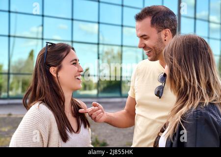Three happy friends talking taking a conversation on the street in a sunny day with buildings in the background. High quality photo Stock Photo