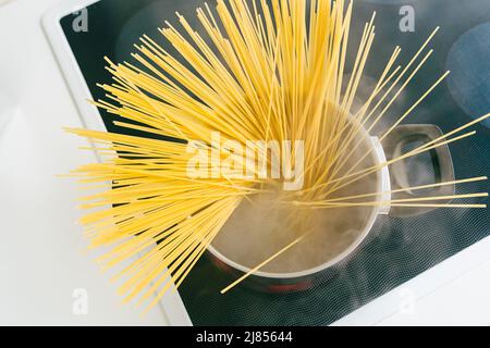 Spaghetti in pot is cooked in boiling water on electric ceramic hob. Top view, soft focus, yellow gluten free corn pasta cooking bolognese Stock Photo