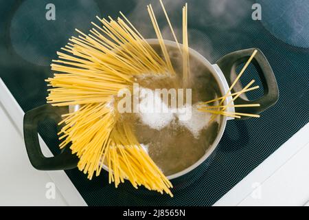 Spaghetti in pot is cooked in boiling water on electric ceramic hob. Top view, soft focus, yellow gluten free corn pasta cooking bolognese Stock Photo