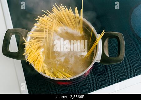 Spaghetti in pot is cooked in boiling water on electric ceramic hob. Top view, soft focus, yellow gluten free corn pasta cooking bolognese Stock Photo
