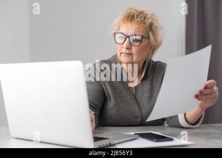 An elderly woman fills a receipt for payment of utility bills. Stock Photo