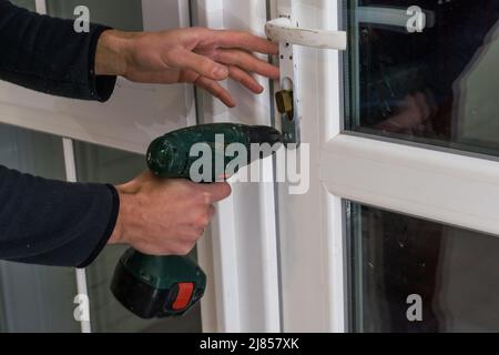 Handsome man using a screwdriver to install a window handle and looking at the camera. Making a house cozy and warm Stock Photo