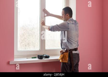 Handyman using a cordless screwdriver to install a window handle. Qualified worker services, home repair and renovation. Stock Photo