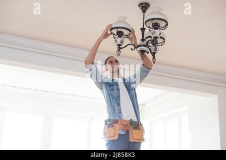 An electrician fixing wires, installing light on the ceiling Stock Photo