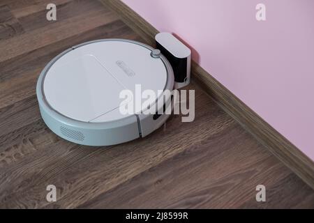 Robotic vacuum cleaner on laminate wood floor charging from base station. Smart cleaning technology. robot vacuum cleaner return to charging at dock Stock Photo