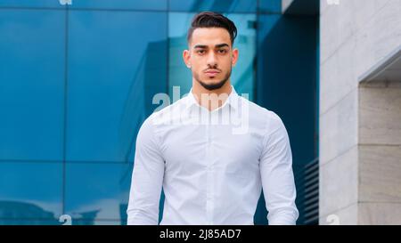 Serious hispanic arabic indian businessman standing in formal clothing near modern building background. Confident successful bearded man guy posing at Stock Photo