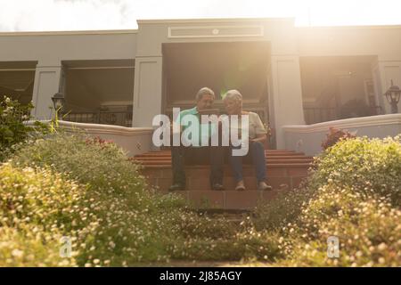 Low angle view of biracial senior man showing digital tablet to wife while sitting on steps Stock Photo