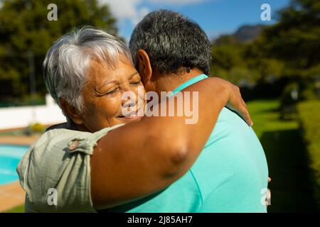 Close-up of biracial senior woman with eyes closed embracing husband in park during sunny day Stock Photo