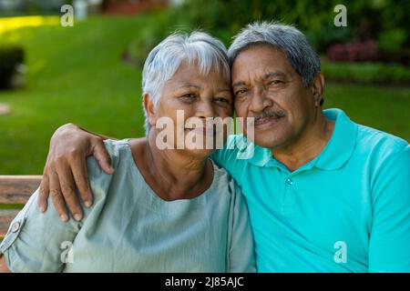 Close-up portrait of loving senior man with hand on wife's shoulder sitting on bench in park Stock Photo