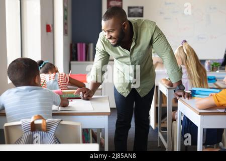 Smiling african american young male teacher talking to african american elementary boy at desk Stock Photo