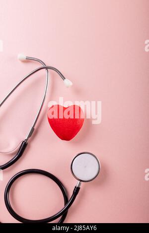 Overhead view of stethoscope with red heart shape against pink background, copy space Stock Photo