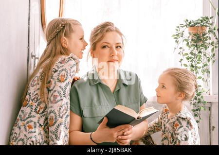 happy family mother with cute little kids daughters girls have fun together in suburb countryside home on sunny summer day. candid mom hugging and rea Stock Photo