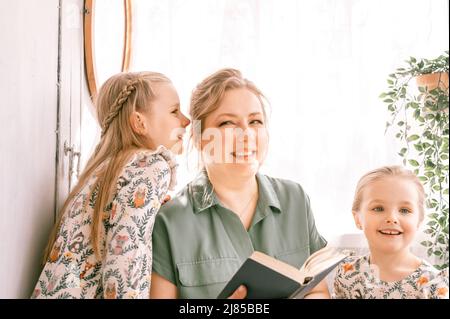 happy family mother with cute little kids daughters girls have fun together in suburb countryside home on sunny summer day. candid mom hugging and rea Stock Photo