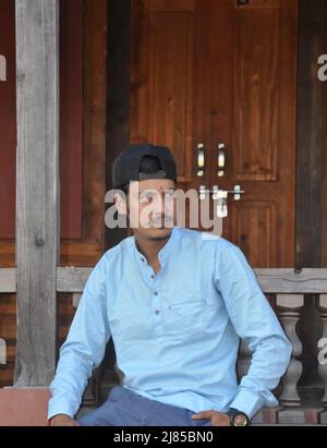 A good looking Indian young guy with wearing cap backwards, looking sideways while sitting in temple Stock Photo