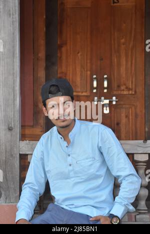 A good looking north Indian young guy with wearing cap backwards, looking at camera while sitting in temple Stock Photo
