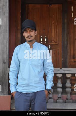 Front view of a north Indian young guy wearing cap backwards and posing with hands on pocket, looking at camera while standing in temple Stock Photo