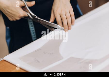 The tailor cuts out the fabric according to the pattern, close up. Fabric cutting. Profession of tailor and cutter, small business Stock Photo