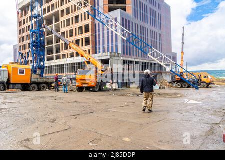 Kemerovo, Russia - June 22, 2021. Work at construction site: finishing facade of frame building under construction and dismantling tower crane for tra Stock Photo