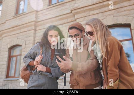 Below view of excited young multi-ethnic friends using online map on smartphone while checking their route, lens flare effect Stock Photo