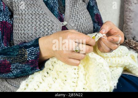 Housewife knitting at home, woman knitting sweater with white thread, hand-knitted concept, a hobby of old women, side view Stock Photo