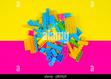 Colorful blocks toy, colored background, playing and learning concept, spilled kid toys, building blocks, yellow and pink backdrop, top view Stock Photo