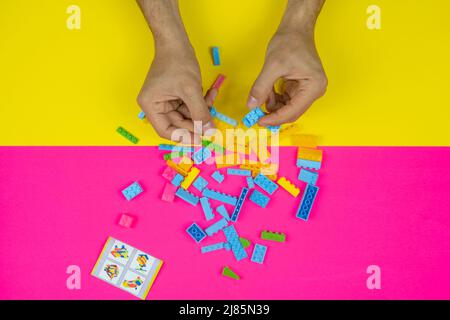 Hand playing with colorful lego blocks toy, colored background, top view, playing and learning concept, bunch of lego block, spilled kid toys Stock Photo