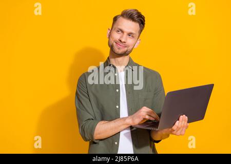 Portrait of attractive minded smart clever cheerful guy using laptop thinking copy space isolated over bright yellow color background Stock Photo