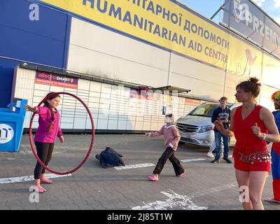 Przemysl, Poland. 12th May, 2022. Jenni (in red) from Berlin with her hoolah-hoop, a performer with the Mobile Circus For Peace and Cabuwazi, traveling circus for children, plays with the refugee children and amuses adults at Tesco, a Ukrainian Humanitarian aid processing center in Przemysl, Poland, near the Medyka Border, bringing laughter to hundreds of grief-stricken people who have just arrived at the welcoming Polish border town from Kharkiv, Kiev, Odessa and other places under seize by Russian invaders. (Credit Image: © Amy Katz/ZUMA Press Wire) Stock Photo