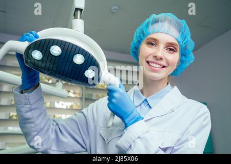 Portrait of smiling female surgeon in surgical uniform at operating room posing near operational light in laboratory Stock Photo