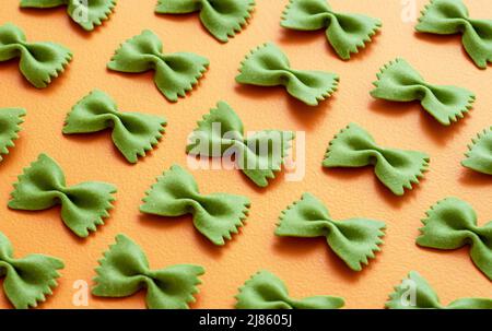 Spinach farfalle pasta aligned symmetrically on an orange table. Close-up with uncooked bow tie-shaped pasta. Stock Photo