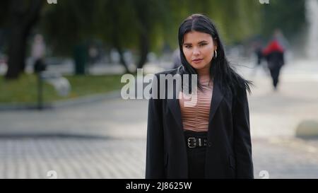 Young confident serious hispanic businesswoman in business suit standing outdoors near roadway pedestrian crossing girl leader employee manager office Stock Photo