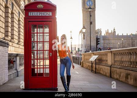 A tourist woman takes selfie pictures at a red telephone booth in London Stock Photo